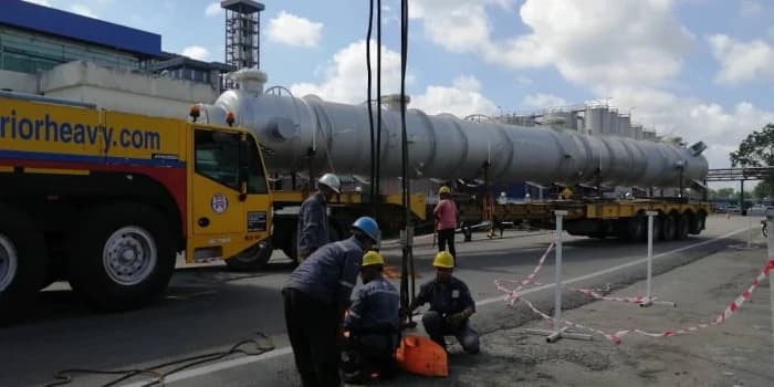Team rigging a large industrial vessel for transport with a multi-axle trailer