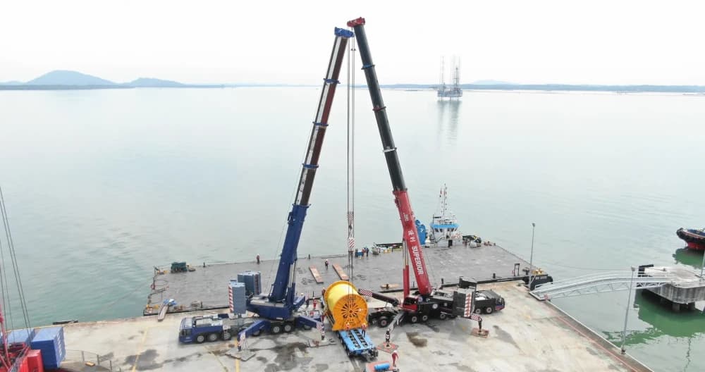 Tandem lift of a large industrial reel at a port by two Demag AC700 mobile cranes